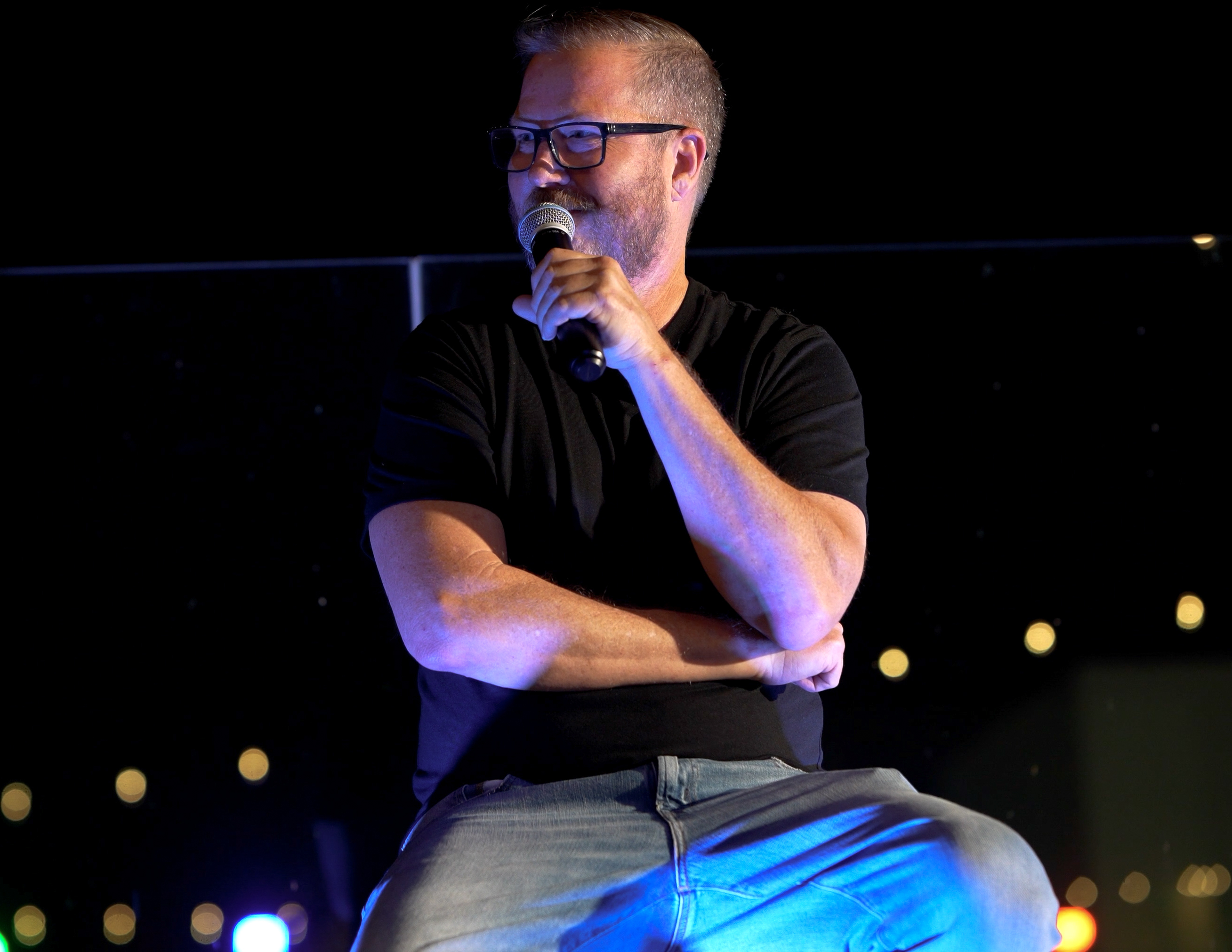 Live comedy event photograph of a comedian speaking into a microphone under blue stage lighting by Big Rich Visuals