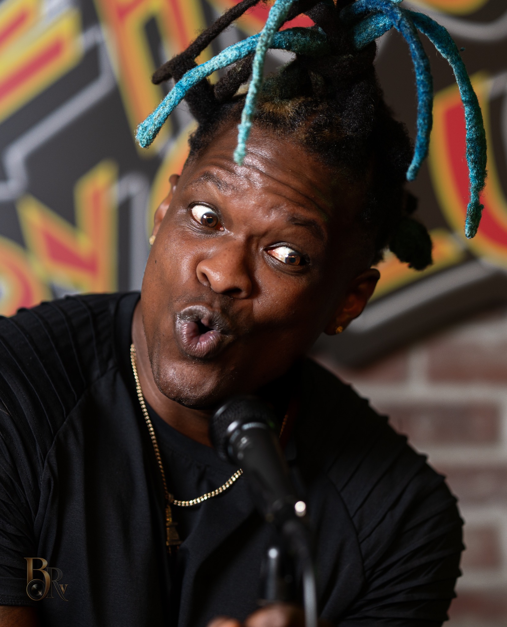 Expressive comedian portrait with microphone, colorful hair, and playful facial expression by Big Rich Visuals