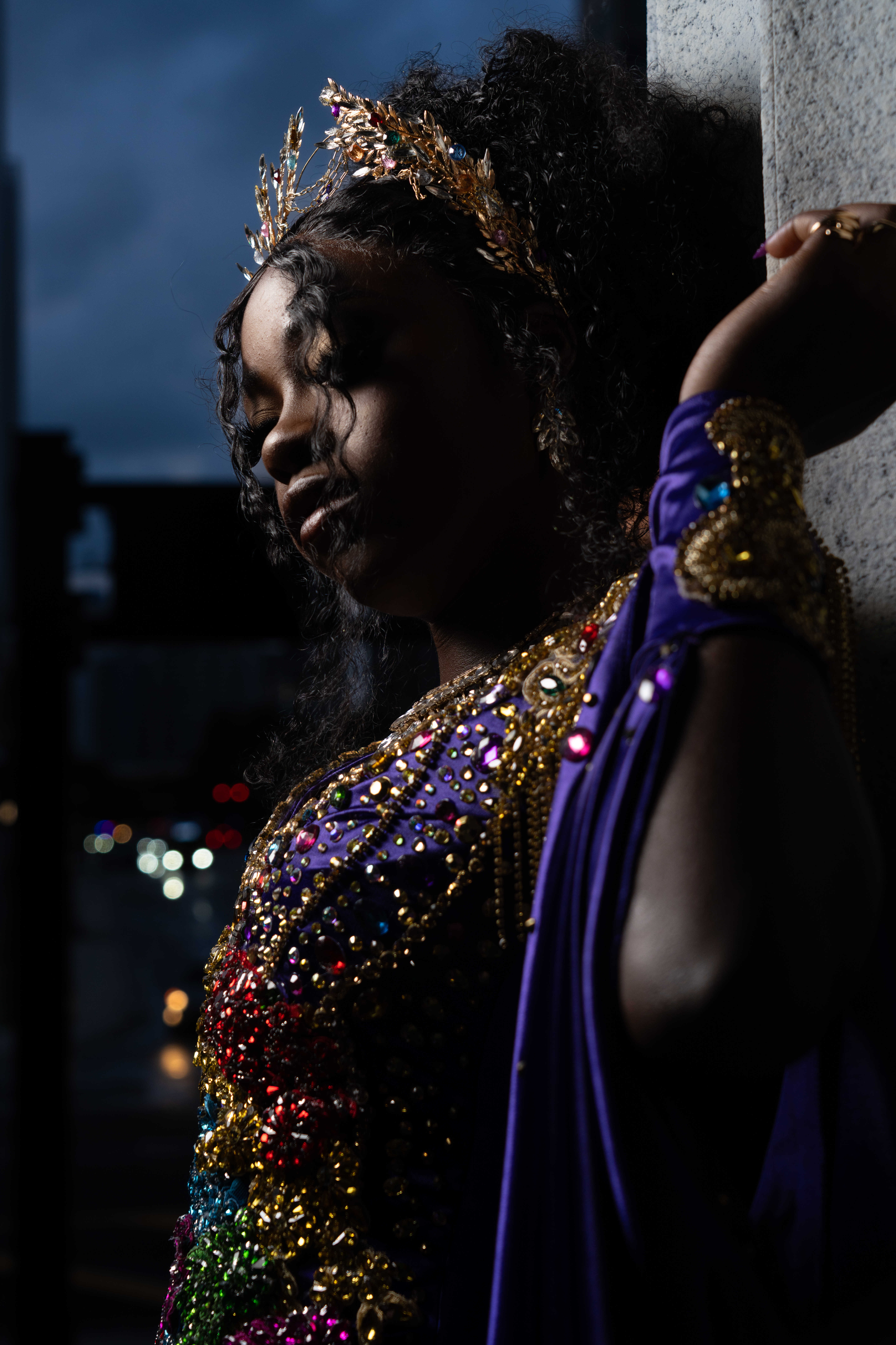 Dramatic high-fashion portrait of a woman in a jeweled purple gown leaning against a wall at night by Big Rich Visuals